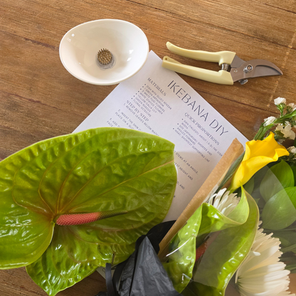 Floral arrangement tools and materials on a wooden table with a 'Ikebana DIY' book.